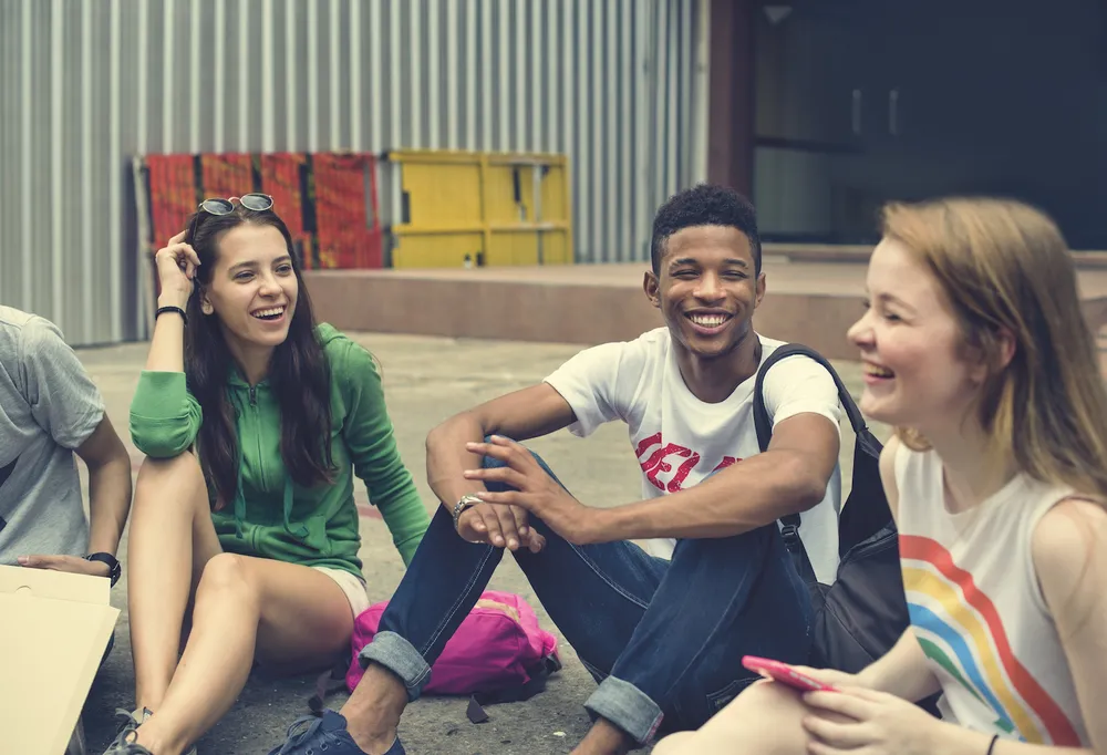Group of happy teens sitting in a circle on the ground and laughing