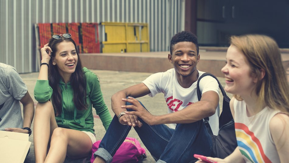 Group of happy teens sitting in a circle on the ground and laughing