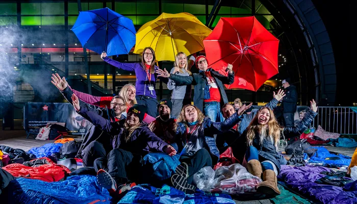Group of people at Byte Night event. They are outside, Smiling and laughing and are surrounded by sleeping bags and umbrellas