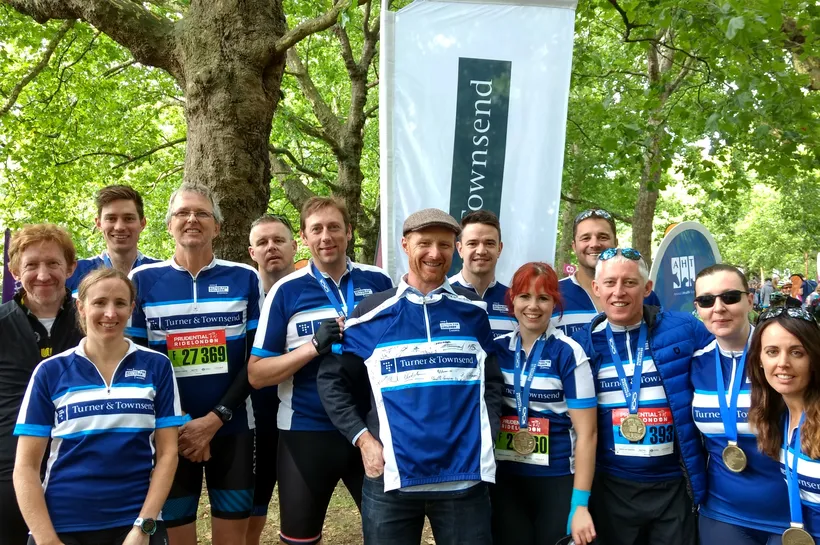 Group of people stanidng under some trees, wearing Turner & Townsend branded cycling tops