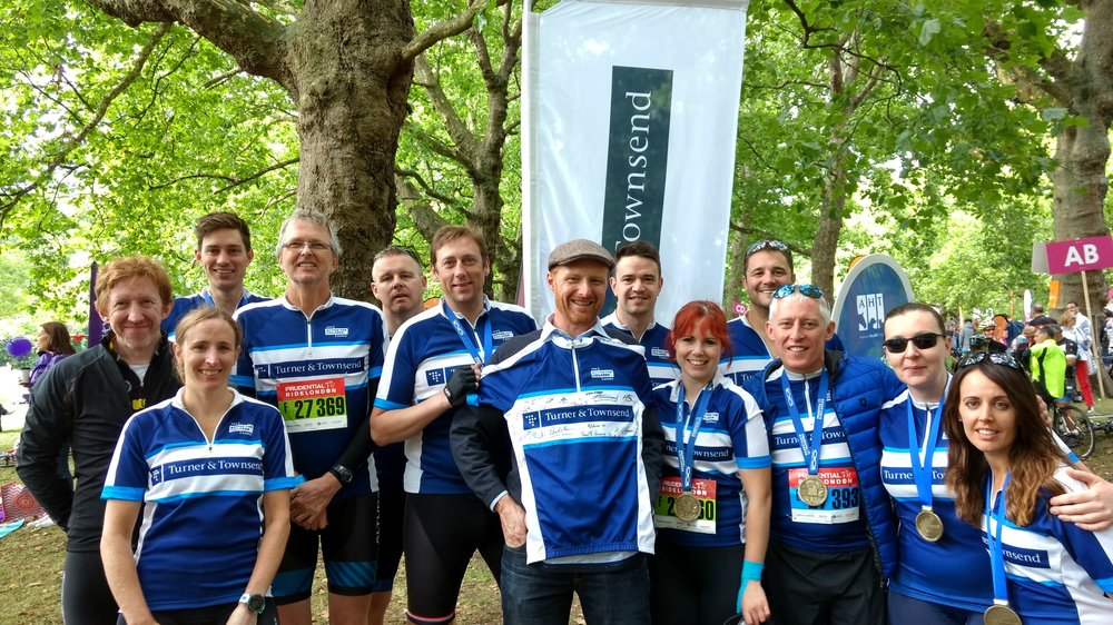 Group of people stanidng under some trees, wearing Turner & Townsend branded cycling tops