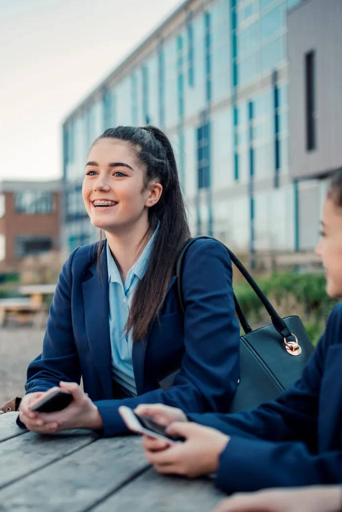 A group of schoolgirls sit talking at a table outside of school