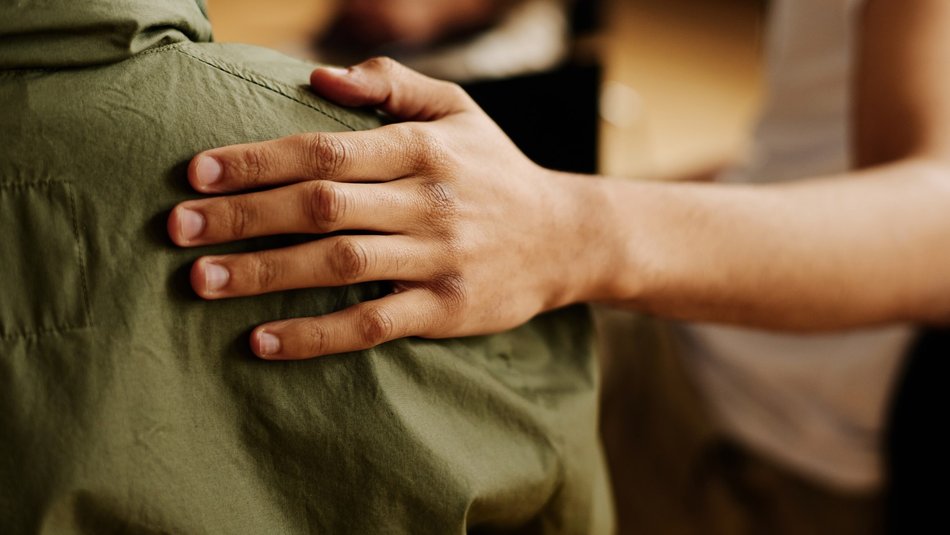 Comforting hand on right shoulder of young person wearing a green jacket