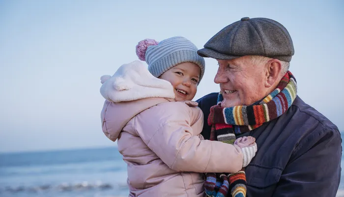 Happy grandfather and toddler hugging on the beach