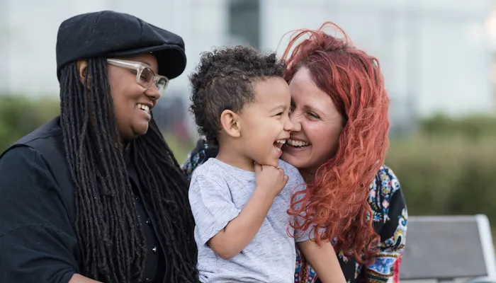 Happy mothers sitting and laughing on a bench with young son