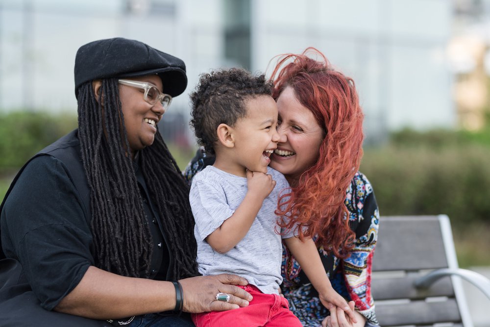 Happy lesbian mothers sitting and laughing on a bench with young son