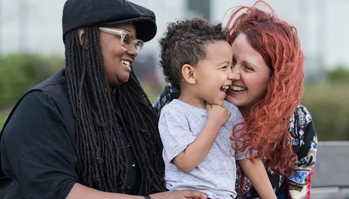 Same‑sex couple laughing and playing with their foster child, showing the joy of fostering