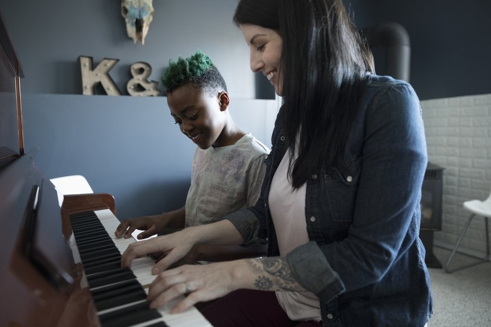 Happy woman and young girl sat playing piano together