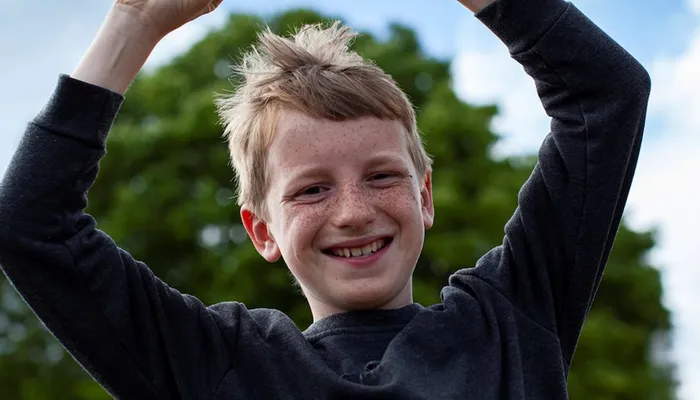 Happy young boy throwing arms in the air and smiling at the camera