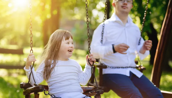 Happy young sister and older brother playing on the swings