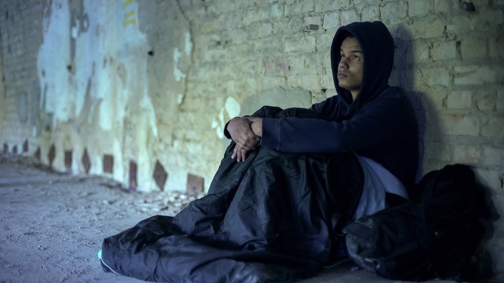 Homeless teenager in a sleeping bag preparing to sleep on the street.jpg