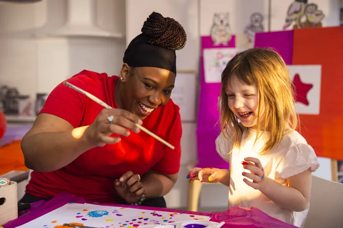 Abby, a young girl, is doing therapy play crafts with her support worker. They are both smiling and laughing.