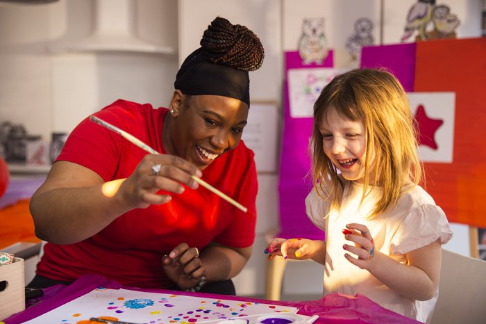 Abby, a young girl, is doing therapy play crafts with her support worker. They are both smiling and laughing.