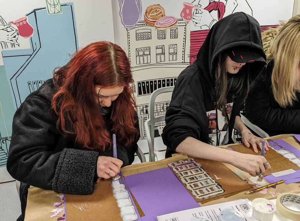 Two young people participating in out intro to customer services programme. They sitting down at a table and painting.