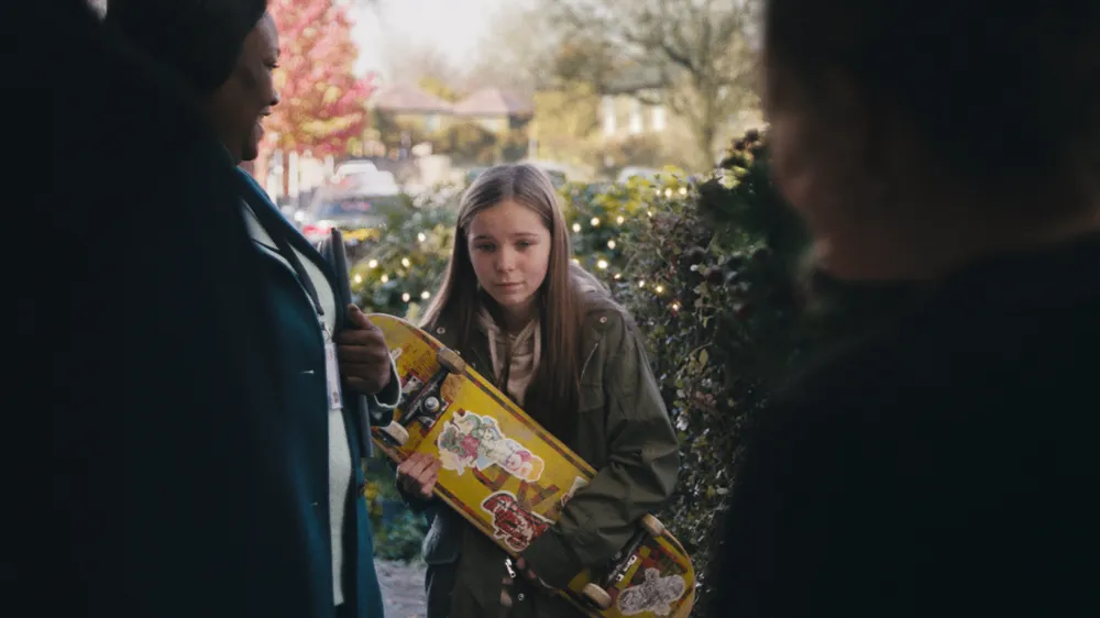 Young girl holding skateboard standing at the door look down at floor as she meets her new foster carers in John Lewis Christmas Ad