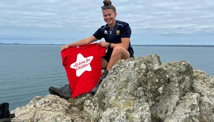 AFC fundraiser Lauren sits on top of a cliff after a challenge, holding an AFC branded tshirt