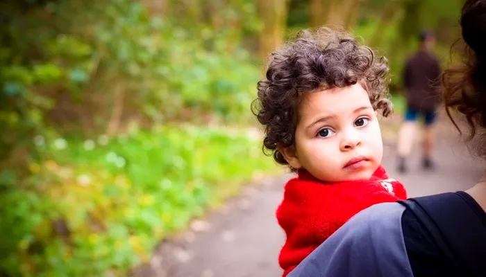 Young girl in a red jumper being carried by her mother looking back at the camera