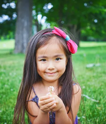 Little girl with long hair standing in field holing flower