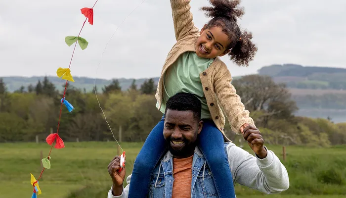 Carer with a foster child on his shoulders flying a kite, reflecting the happiness fostering can bring