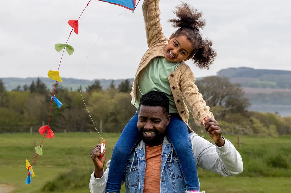 Carer with a foster child on his shoulders flying a kite, reflecting the happiness fostering can bring