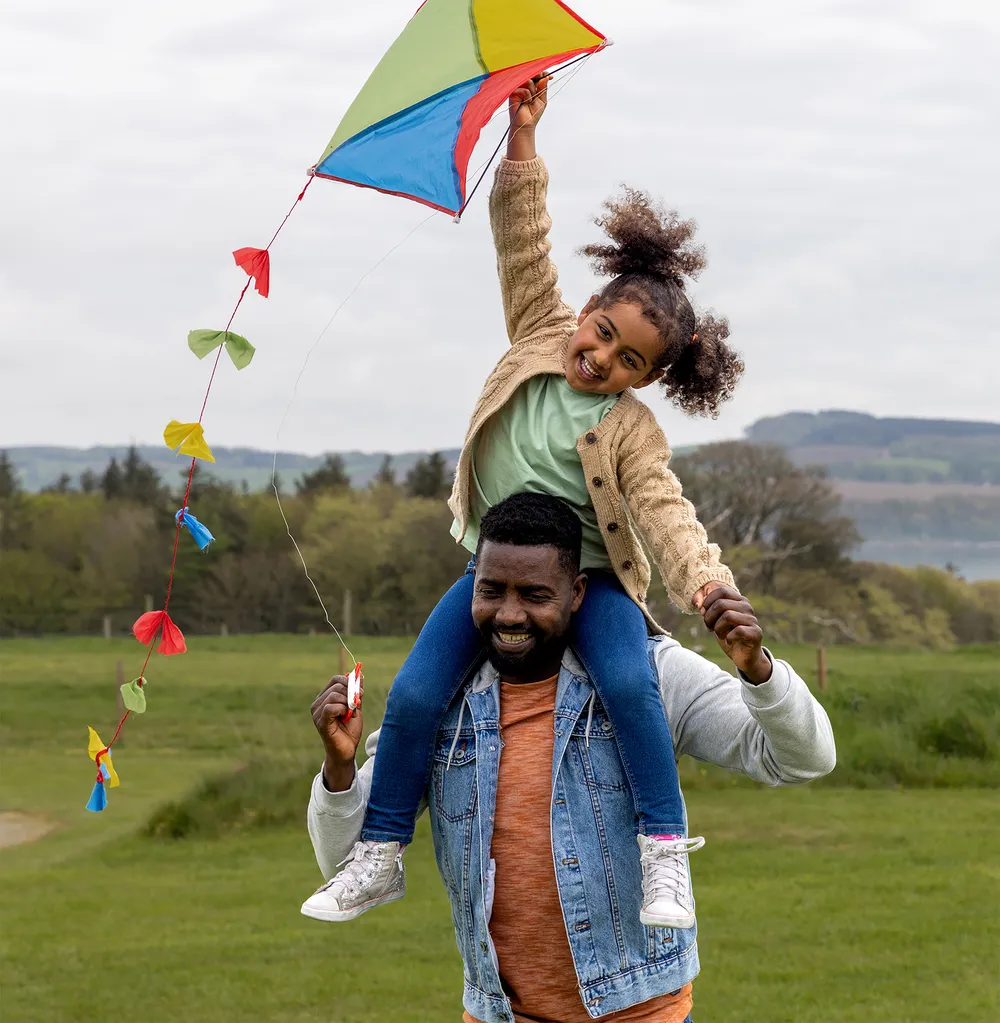 Carer with a foster child on his shoulders flying a kite, reflecting the happiness fostering can bring