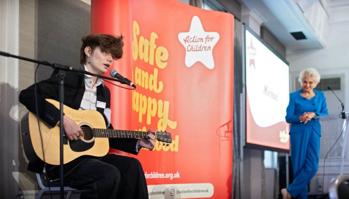 Young man playing the guitar and singing into a microphone while sitting on a stage