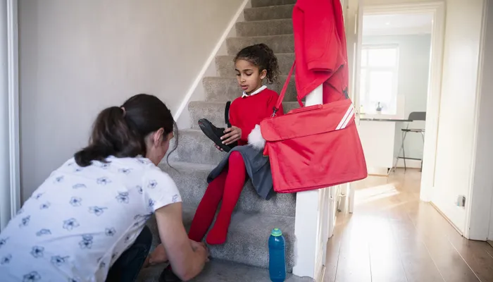 Mother helping her daughter put on school shoes