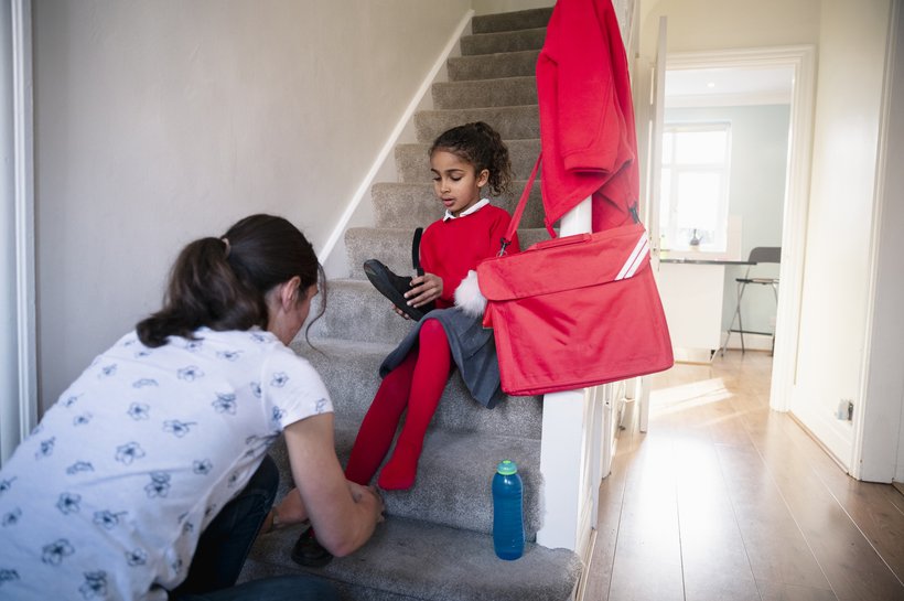 Mother helping her daughter put on school shoes
