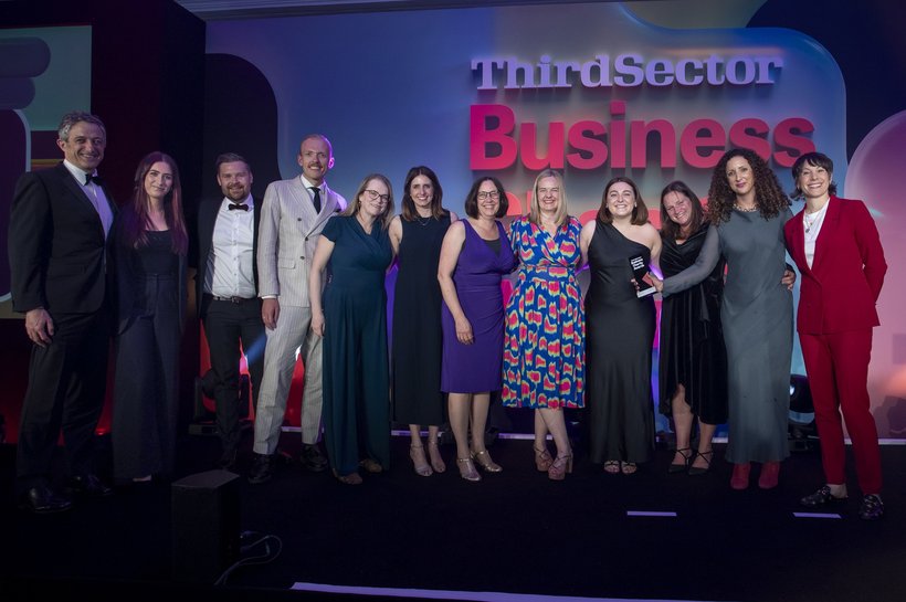 A group of people in smart clothing standing in front of a blue backdrop with the word 'business' in large red letters
