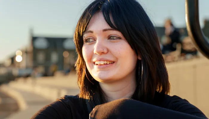 A young woman with sunshine and a hopeful expression on her face, wearing a black shirt
