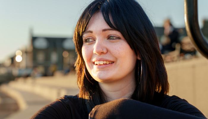 A young woman with sunshine and a hopeful expression on her face, wearing a black shirt