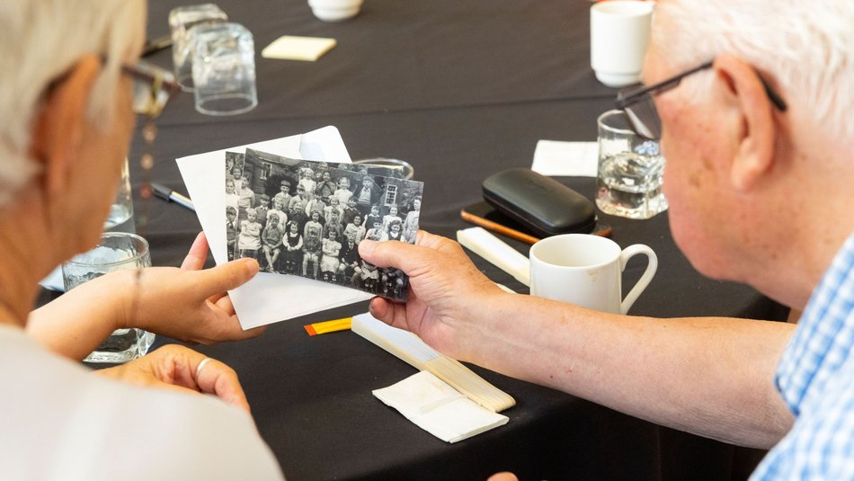 Two older people looking at black and white photograph of children