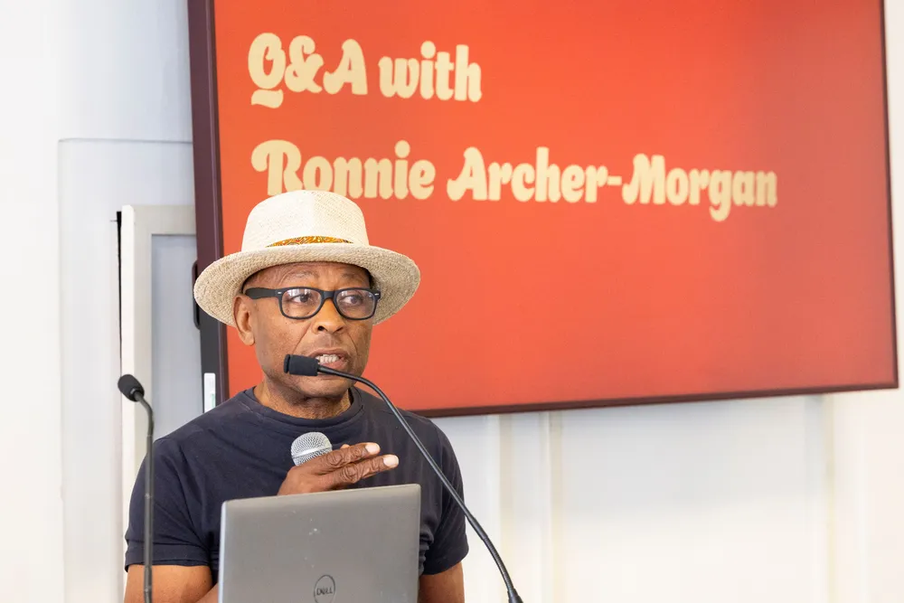 A man speaking at a microphone stand wearing a white hat