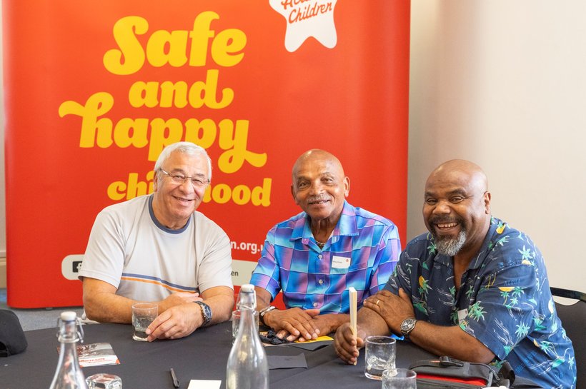 Three older men sitting at a table smiling for a photo