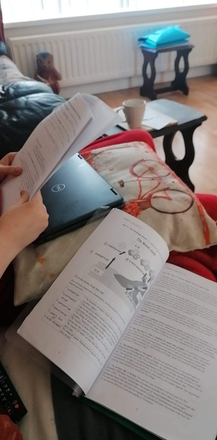 Open school books on the laps of two teenagers at home in their living room