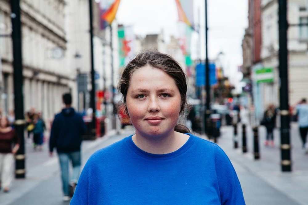 Portrait of Angharad in blue t-shirt standing in the middle of a high street