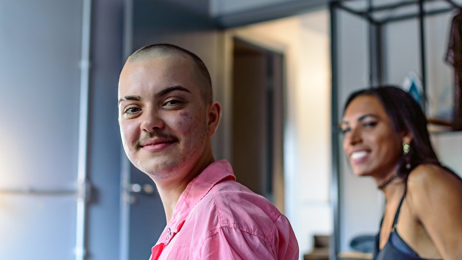 Portrait of a non-binary person smiling looking into the camwera and a transgender woman looking at the them