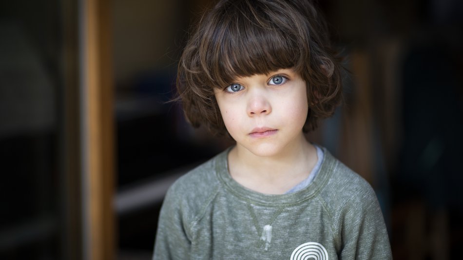 Young worried boy with long brown hair looking into the camera