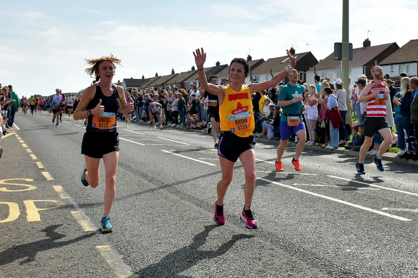 Rhona, woman in Action for Children t-shirt, cheers to the crowd as she runs the great north run for Action for Children