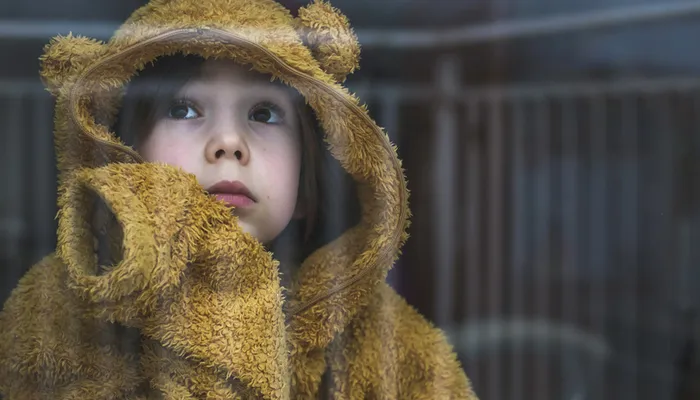 Sad cold child wearing yellow jumper looking out window