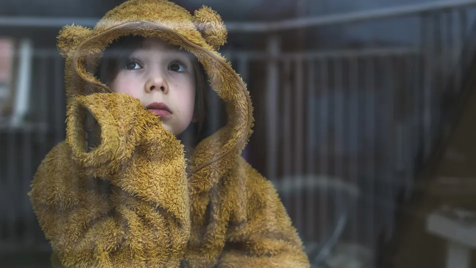 Sad cold child wearing yellow jumper looking out window