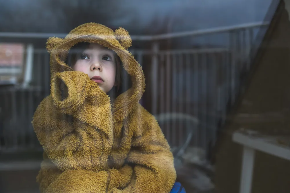 Sad cold child wearing yellow jumper looking out window