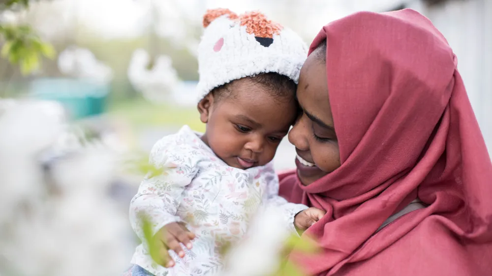 Samira, a woman in a red hijab smiles while looking at her baby daughter
