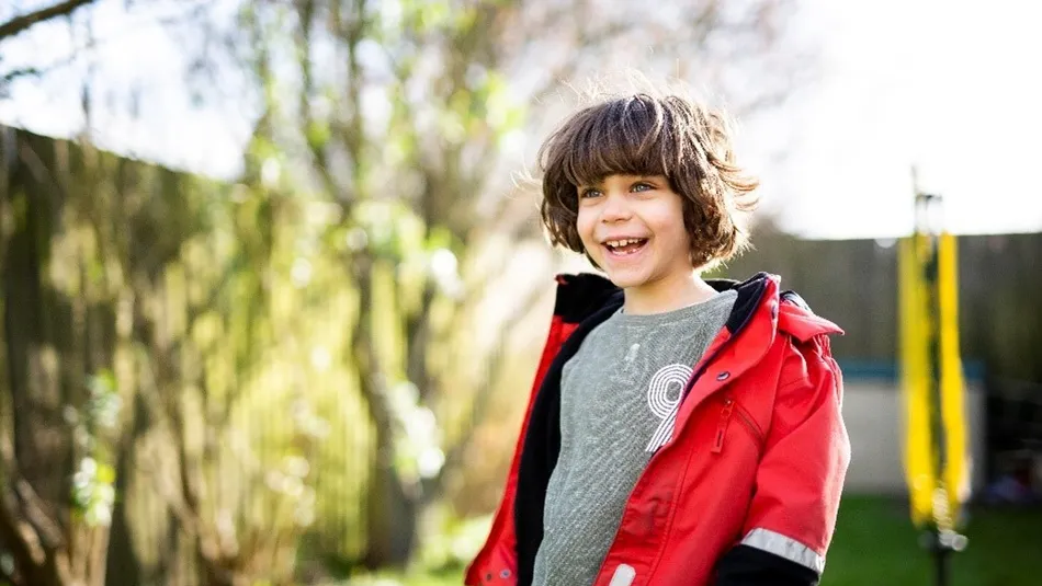 Smiling young boy outside wearing a red coat.