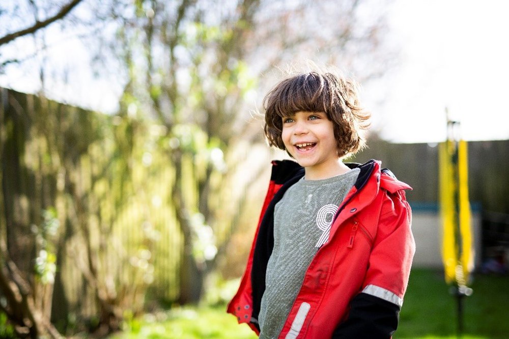 Smiling young boy outside wearing a red coat.