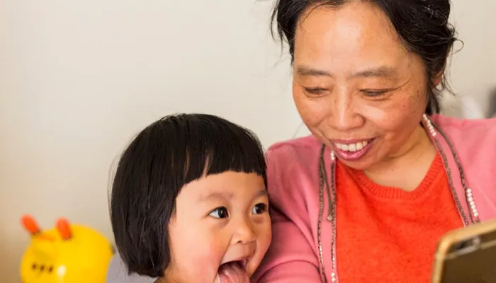 Little girl sitting on sofa with mother looking at smart phone
