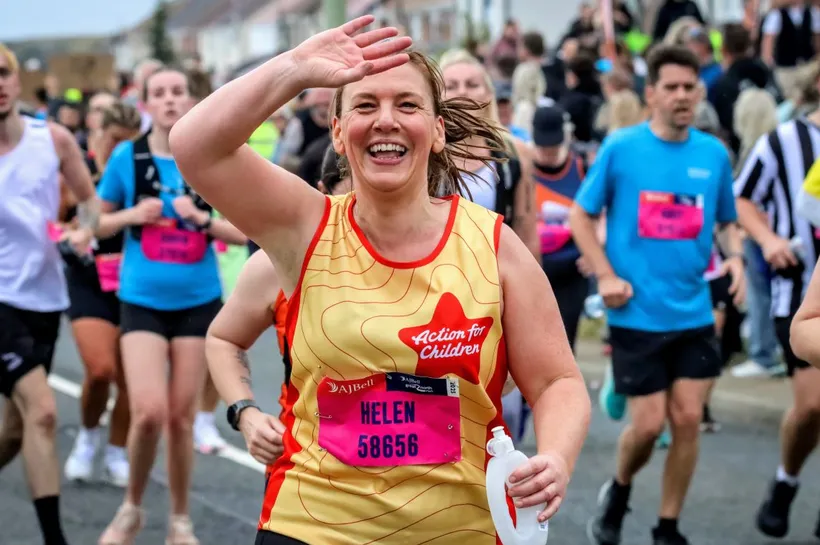 An Action for Children runner, running a half marathon and waving at the camera