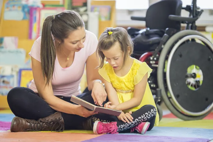 Teacher and young girl sitting on the ground reading a book together.jpg