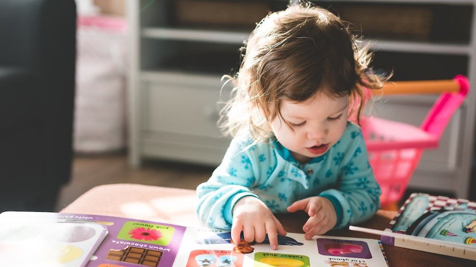 Toddler sat at coffee table reading childrens books