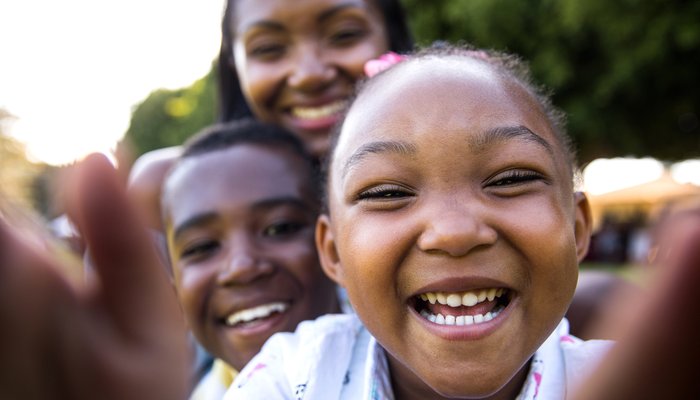 Two laughing children taking a selfie with their mother smiling in the background